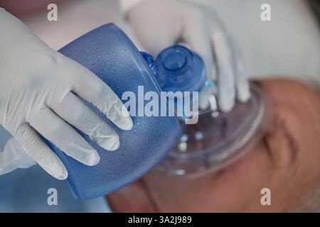 Administering oxygen to a patient using a medical mask and gloves in a clinical setting. Medical procedure being facilitated for respiratory support Stock Photo