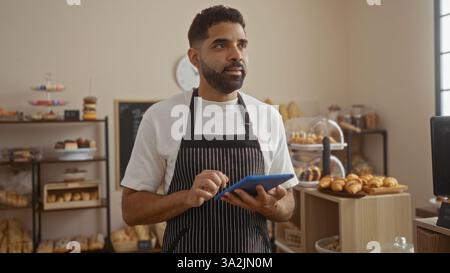 Handsome young man in a bakery using a tablet to manage orders in an indoor setting Stock Photo