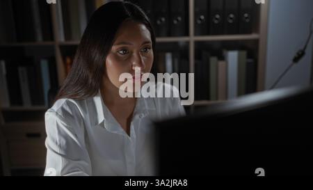 Brunette woman working indoors in an office with focus on her as she looks intently at a computer screen Stock Photo