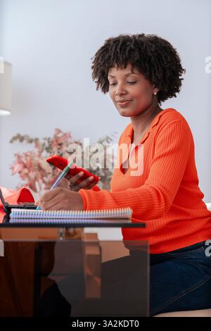 African American student using smartphone while studying at home with laptop Stock Photo