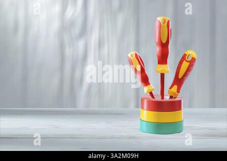 Three red yellow insulated electrical screwdrivers standing in stack of rolls insulation tapes vintage white painted wooden background Stock Photo