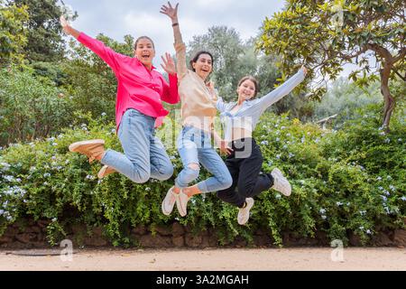 Three joyful young women jumping in the air, celebrating and having fun outdoors. Stock Photo
