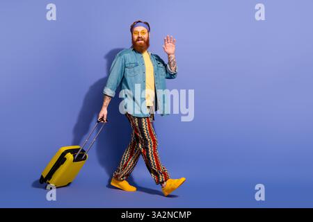 Smiling bearded man with red hair posing stylishly in colorful casual outfit against a purple background Stock Photo