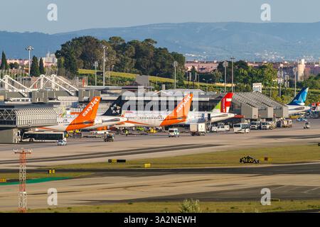 Lisbon, Portugal - Apr 24, 2024: TAP, Azores Airlines and EasyJet airplanes in Lisbon airport ready for boarding and takeoff on sunny day, clear blue sky. Ground support vehicles, airport Terminal 1 infrastructure, city buildings in background.  Stock Photo