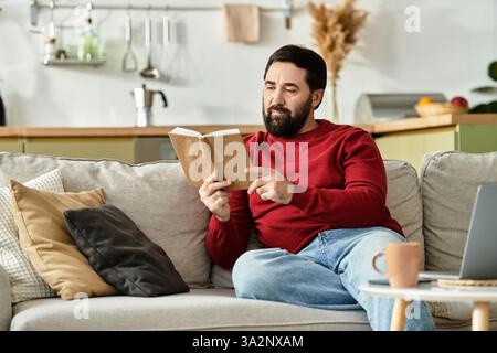 An attractive older man relaxes on a cozy couch, absorbed in a book during his leisure time. Stock Photo