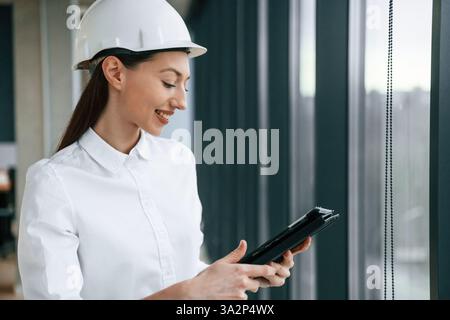 Female architect in hard hat and in white clothes is indoors. Stock Photo