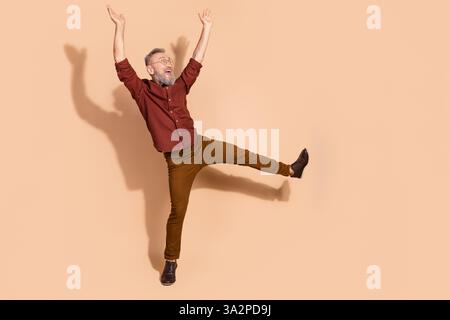Elderly man joyfully posing against beige background, wearing elegant attire and demonstrating an energetic and vibrant personality Stock Photo