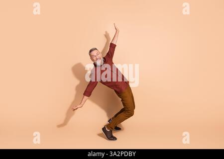 Elderly man in casual attire striking a playful pose against a beige background expressing enjoyment and positive energy Stock Photo