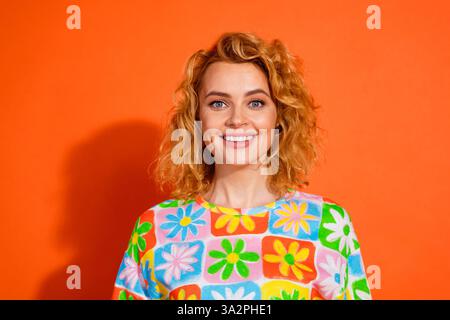 Smiling young woman wearing a colorful floral print top against a vibrant orange background, exuding positivity and bright summer vibes. Stock Photo