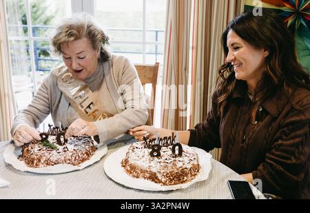 Happy elderly mother and her daughter sharing a joyful moment in front of birthday cakes for her 80th celebration. Stock Photo