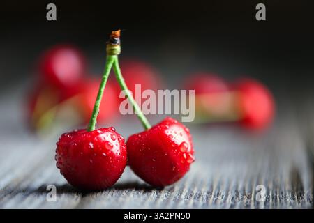 Macro shot of two ripened red cherries with water droplets on rustic wooden table. Food photography Stock Photo