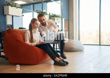 Sharing new ideas, showing information in laptop. Man and woman employees are working in the office. Stock Photo