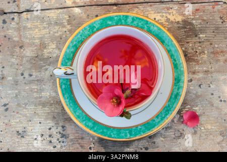 in the background a ruined vintage table, above an antique teacup decorated in gold and green containing red tea where you can see reflections and the Stock Photo