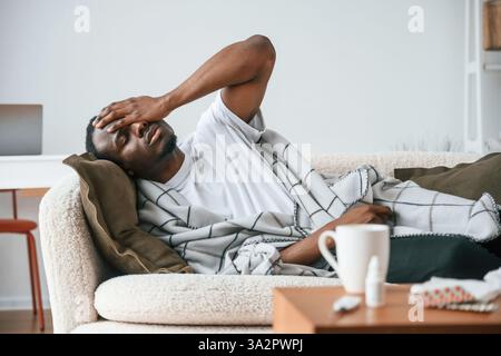 Lying down on the sofa. Sick black man is at home. Stock Photo