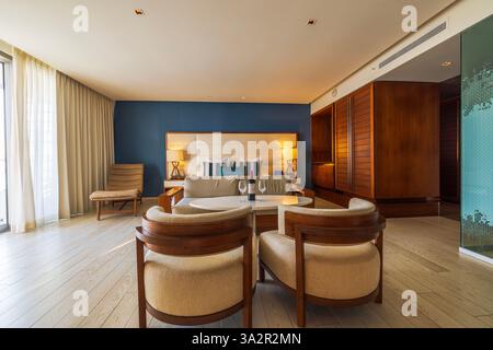Luxury hotel suite with modern wooden furniture, large bed, blue accent wall, and elegant seating area with wine bottle. Cancun. Mexico. Stock Photo