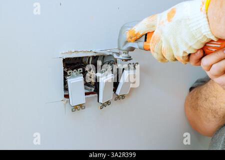 Individual works on repairing multiple light switches in wall, ensuring proper electrical function. Stock Photo