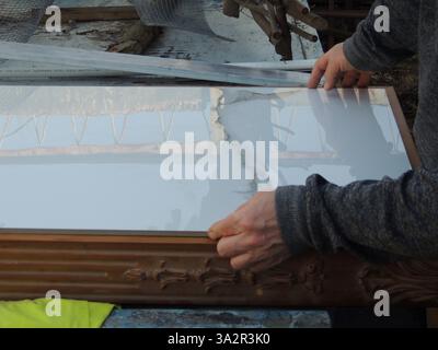 man's hands carefully placing heavy marble slab into wooden frame, close-up, inserting decorative glossy large tile into carved wood frame Stock Photo