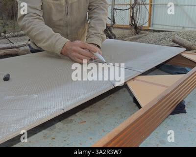 tiler draws a line with a marker on a large finishing tile using a ruler, marking on building material in a craftsman's workshop, marking tiles Stock Photo