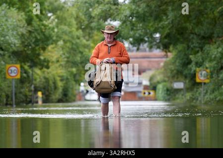 A man makes his way along a flooded road in Offord Cluny, Cambridgeshire. Further showery spells are expected across England, but drier, more settled weather conditions are set to arrive in the coming days. Picture date: Wednesday October 2, 2024. Stock Photo