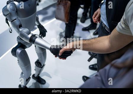 A humanoid robot by the company Unitree is seen shaking hands with people in a handshake. Concept of human and robots interaction and robotics enginee Stock Photo