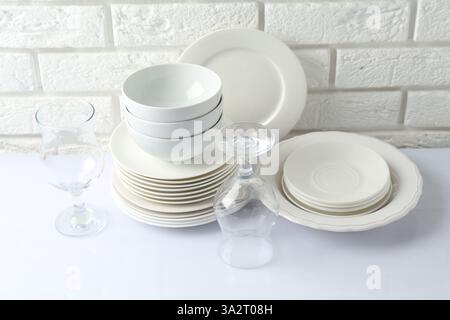 Different clean dishware on white table near brick wall Stock Photo