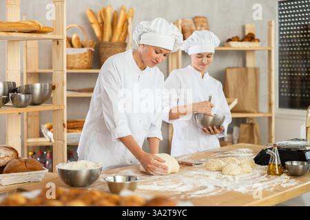 Female bakers in uniform preparing gray dough Stock Photo
