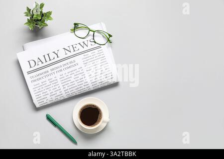 Daily newspaper with glasses, cup of coffee and plant on grey background Stock Photo