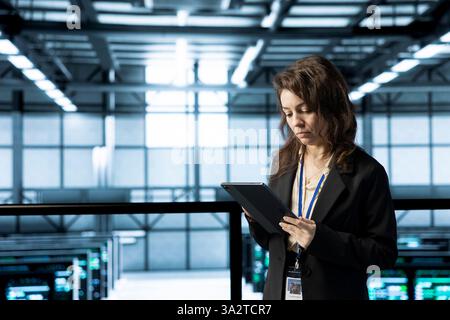 System administrator in data center uses automation tools on tablet, running predictive maintenance routines. IT expert ensuring continuous uptime of server farm, managing data flows with device Stock Photo