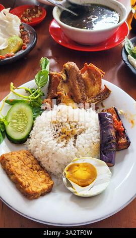 East Javanese food Ayam Penyet with eggplant and red chilli sambal, fried tempeh, and a boiled duck egg. Stock Photo