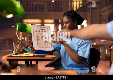 Future nurses studying anatomy class notes in a university library, reviewing courses and preparing for exams. Black med school students working together for their medical careers. Stock Photo