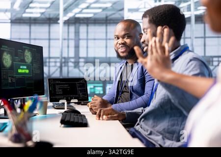 Cheerful engineer in data center getting access granted notification on PC screen, managing to access server files after they were locked by hacker using ransomware, receiving help from colleagues Stock Photo