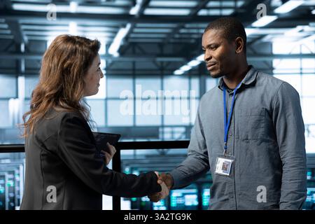 Data center admin meeting with supervisor verifying workspace security. Server room IT employee doing welcoming handshake with inspector arriving in facility to scan infrastructure Stock Photo