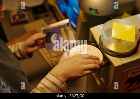 Person holding photo near printer while placing document on scanner in office. Multiple devices surrounding work area, showing busy environment without visible person Stock Photo