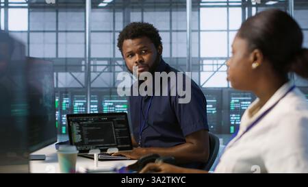 IT specialists in data center doing brainstorming, maintaining company network infrastructure. Team of server hub computer scientists chatting, ensuring optimal system performance, camera A Stock Photo