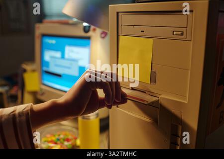 Hand inserting floppy disk into vintage computer with background showing another computer monitor displaying a blue screen. Scene capturing nostalgia of retro technology Stock Photo