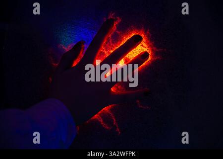 Orange plasma filaments reaching out to a child's hand interacting with a plasma ball exhibit, creating a mesmerizing display of electricity and scien Stock Photo