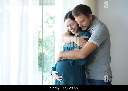 Happy interracial couple enjoying pregnancy looking at belly in a house Stock Photo