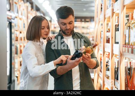 Choosing between two different bottles. Man and woman in the wine shop. Stock Photo
