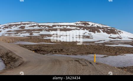 Dirt winding road through the rugged mountains covered with snow in Westfjords, Iceland. Stock Photo