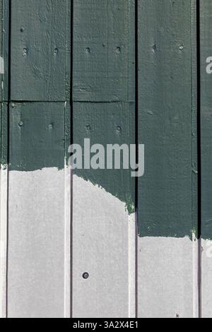 A close-up of painted wooden planks on a building facade, with uneven white and green layers revealing brush marks and imperfect coverage Stock Photo