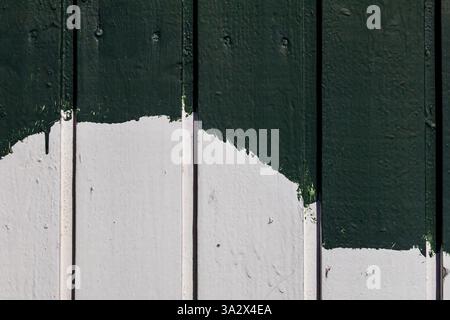 A close-up of painted wooden planks on a building facade, with uneven white and green layers revealing brush marks and imperfect coverage Stock Photo
