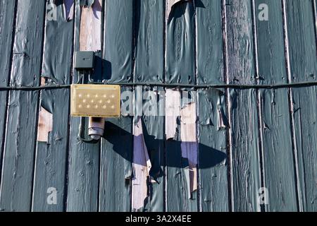 green paint peeling from a wooden plank facade, with an electrical cable running across it, also coated in the same weathered layer, revealing age Stock Photo
