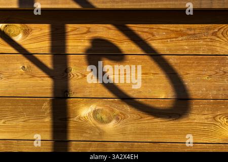 A shadow of a coiled rail falls across an outdoor wooden plank wall, highlighting the visible wood grain and natural texture in soft, Stock Photo