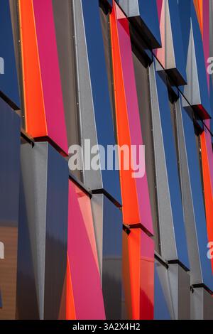 A modern building facade composed of red and dark blue metal rectangles, offset to reveal black canvas sun screens, creating a dynamic contrast Stock Photo