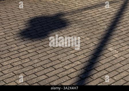 The shadow of a lamp post falls diagonally across cement paving slabs, neatly set in sand, highlighting the clean lines and subtle texture Stock Photo