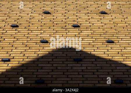 A yellow brick building facade features raised rectangular black iron elements, echoing the brick pattern but shorter and protruding, adding depth Stock Photo