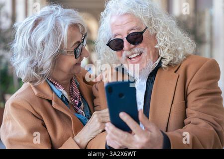 Happy senior couple using smartphone together, smiling and enjoying technology. Stock Photo