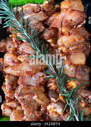 Grilled marinated chicken pieces ready for cooking with fresh herbs on a black platter Stock Photo