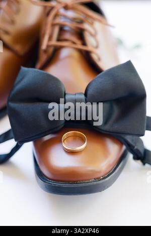 Brown leather shoe with black bow tie and gold wedding ring on top. Stock Photo