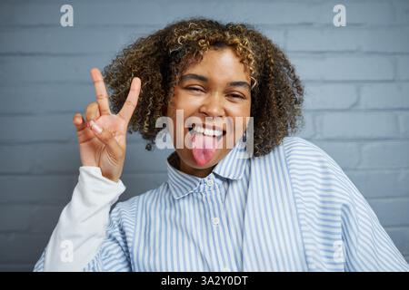 Cheerful Young Woman Smiling and Making Peace Sign Pose Against a Brick Wall Background Stock Photo